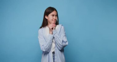 Endişeli bir yüz ifadesi olan kız, mavi arka planda dalgın görünürken ellerini sıktı.