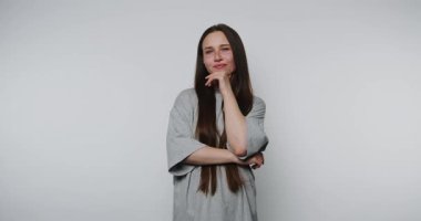 Genç kadın eli çenesinde düşünceli bir şekilde poz veriyor, beyaz arka plan üzerinde derin düşünceler kuruyor.