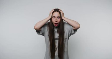 Genç kadın beyaz arka planda başını tutarak şok ve şaşkınlık gösteriyor.