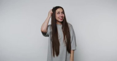 Genç kadın dalgın görünüyor, hafifçe gülümsüyor, başını kaşıyarak, beyaz arka planda merakı somutlaştırıyor.