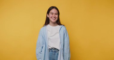 Genç bir kadın sıcacık elbiseler içinde sıcacık bir şekilde gülümsüyor. Ilık ve dostluk saçan parlak sarı arka planda.