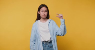 Endişeli genç bir kadın parmaklarıyla hareketler yaparak parlak sarı arka planda küçük bir şey olduğunu gösterir.