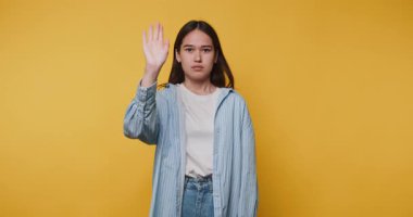 Genç bir kadın, parlak sarı arka planda durmak ya da durmak için elini kaldırıyor.