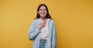 Genç bir kadın neşeli bir ifadeyle içten bir kahkahayı paylaşıyor, gerçek bir mutluluk anını yakalıyor ve canlı sarı arka planda kahkaha atıyor.