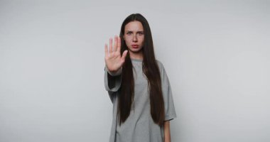 Uzun saçlı kadın, beyaz arka planda vücut dili ve yüz ifadesi ile güçlü bir mesaj ileterek dur hareketi yapıyor.
