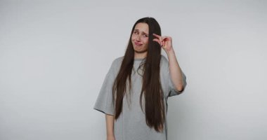 Neşeli bir yüzü olan genç bir kadın, beyaz arka planda gri bir tişört giyerken neşe dolu bir şekilde işaret ediyor ve gülümsüyor.