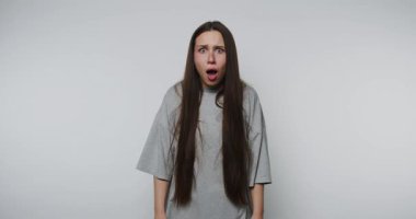 Ciddi bir ifadeye sahip genç bir kadın, beyaz arka planda gündelik gri tişört giyerken endişeyi veya derin düşünceyi simgeleyen tasvir edilir.