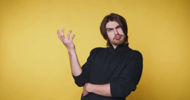 Genç adam şaşkınlığını sarı arka planda sorgulayıcı bir el hareketiyle ifade ediyor.