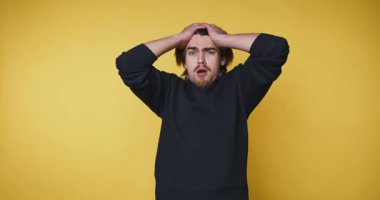 Genç adam kafasını tutarak hayal kırıklığını ifade eder. Sarı arka planda bir stres anı yakalar.