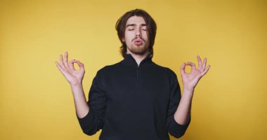 Genç adam, sarı arka planda sakin bir ifadeyle meditasyon yapıyor. Bu sanatsal çekimde sükuneti ve farkındalığı somutlaştırıyor..