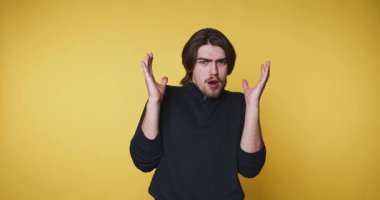 Genç adam öfkeyle ellerini kaldırıyor, sarı arka planda duruyor, hayattaki hayal kırıklığını ve duygusal ifadeyi temsil ediyor.