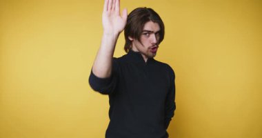 Ciddi genç adam sarı arka planda dur işareti vermek için elini kaldırdı.