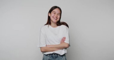 Kollarını kavuşturup gülümseyen genç bir kızın görüntüsü. Hafif arka planda rahatlığı ve kendine güveni somutlaştırıyor.