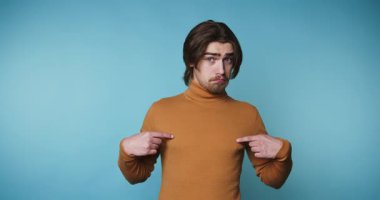 Genç üzgün adamın görüntüsü mavi arka planda ciddi bir ifadeyle kendini gösteriyor.