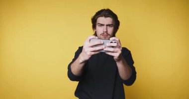 Genç adamın video oyunları oynadığı görüntüler, sarı arka planda bir oyun denetleyicisini tutarken odaklanmış ve kararlı bir ifade sergiliyor