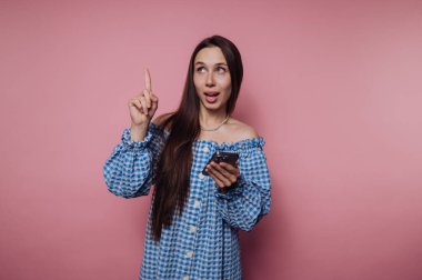 Mavi kareli elbiseli genç bir kadın elinde akıllı bir telefon, yukarı bakıyor..