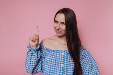 Mavi kareli, omuzları açık gülümseyen kadın pembe arka plana doğru bakıyor..