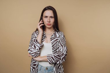 Uzun saçlı, zebra desenli tişörtlü bir kadın telefonda konuşuyor, endişeli görünüyor..