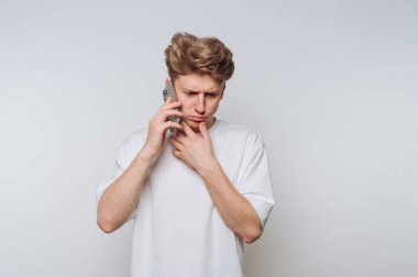 Beyaz tişörtlü genç adam endişeli bir ifadeyle akıllı telefondan konuşuyor..