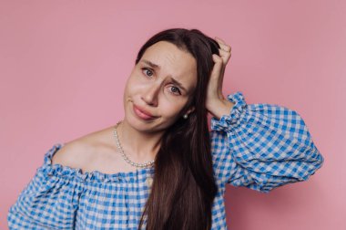 Mavi kareli bluzlu bir kadın pembe bir arka plan karşısında şaşkın görünür..