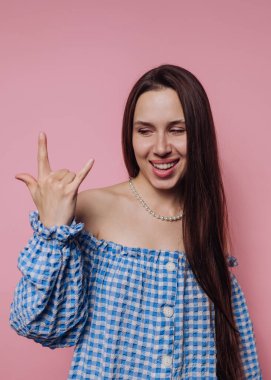 Mavi omuzlu, omuzsuz bir kadın pembe arka planda bir taş el işareti yapıyor..