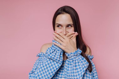 Mavi omuzlu, omuzsuz, ağzı kapalı, elleri pembe arka planda bir kadın..