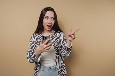 Şaşkın bir kadın elinde akıllı bir telefon tutuyor ve onu işaret ediyor..