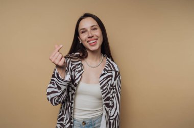 Zebra desenli ceketli gülümseyen kadın parmaklarıyla kalp hareketi yapıyor..