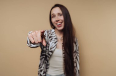 Uzun saçlı, gülümseyen bir kadın bej arka planda kameraya bakıyor..