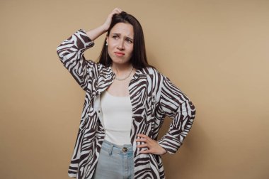 Zebra desenli gömlekli bir kadın kafası karışmış, bej bir arka plana kafasını sürtüyor..