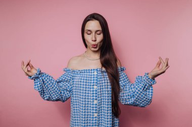 Mavi kareli omuzlu bir kadın pembe bir arka plana karşı neşeli bir ifadeyle poz verir..