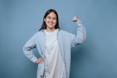 Genç bayan kendine güvenerek gülümsüyor, mavi arka planda kollarını esnetiyor..