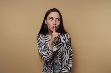Zebra desenli ceketli bir kadın bej bir arka plana karşı şşşş hareketi yapıyor..