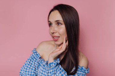 Mavi kareli omuzlu kadın pembe arka planda poz veriyor..