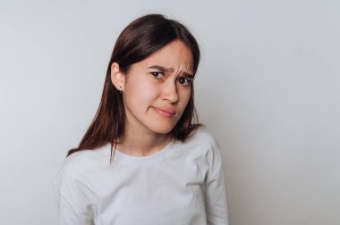 Uzun kahverengi saçlı, beyaz gömlek giyen genç bir kadın şüpheciliğini dile getiriyor..