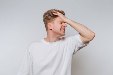 Beyaz tişörtlü genç bir adam. Alnında bir elle hayal kırıklığını ifade ediyor..