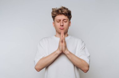 Beyaz tişörtlü, gözleri kapalı ve elleri dua pozisyonunda genç bir adam..