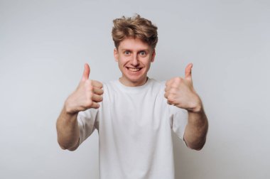 Neşeli bir ifadeyle genç bir adam düz bir arkaplan karşısında iki parmağını kaldırıyor..