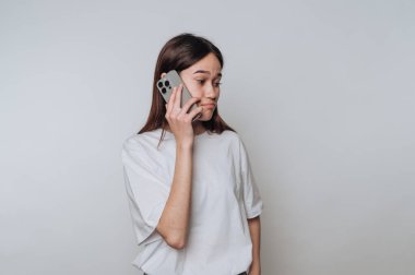 Uzun saçlı genç bir kadın kulağına akıllı telefon dayamış, hoşnutsuz görünüyor..