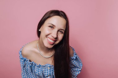 Mavi kareli omuzlu, pembe arka planda gülümseyen bir kadın..