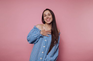 Mavi kareli, omuzları açık, gülümseyen kadın pembe arka planda..