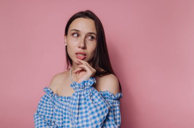Mavi kareli omuzlu, pembe arka planda düşünceli bir kadın..