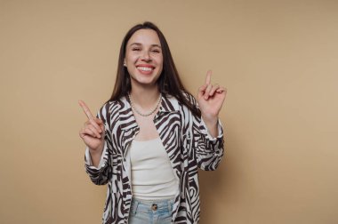 Zebra desenli tişörtlü neşeli bir kadın bej bir arka planı işaret ediyor..