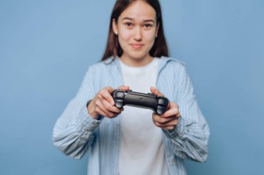 Mavi arka planda oyun kumandası tutan genç bir kadın..