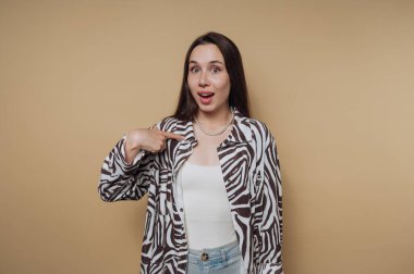 Zebra desenli gömlek ve kot pantolon giyen, bej arka planda kendini gösteren şaşırmış bir kadın..
