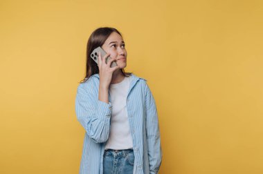 Gündelik kıyafetli genç bir kadın sarı bir arka planda akıllı telefondan konuşuyor..