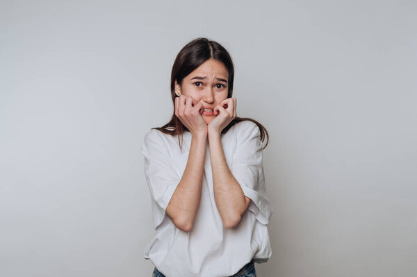 A young woman with a worried expression, biting her nails, against a plain background.