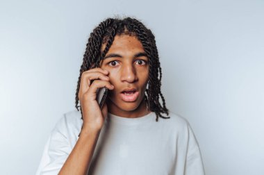 Şaşırmış genç bir adamın portresi telefonda konuşuyor, arka planda beklenmedik haberlerin şaşkınlığını anlatıyor.