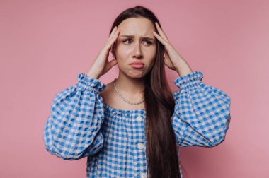 Düşünceli genç bir kadının portresi ellerini başının üstüne koyar, pembe arka planda endişeli bir ifade yakalar.