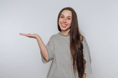 Gri gömlekli genç bir kadının portresi elinde jestler yapıyor, ışık arka planında sıcaklık ve pozitiflik yayıyor.